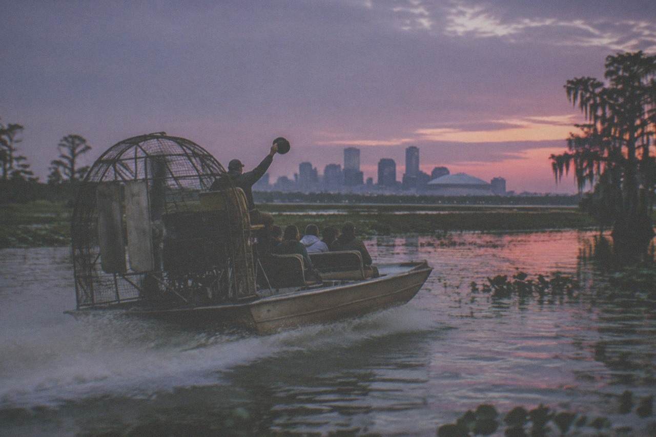 An airboat with its propeller cage gliding across a green Louisiana swamp at dusk