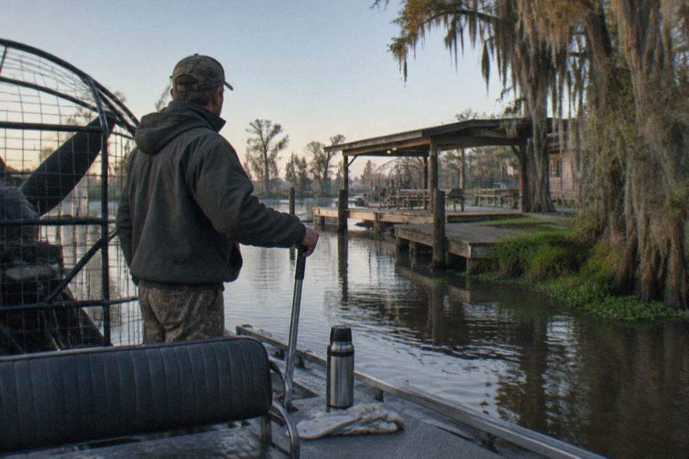 a tour boat captain standing at the helm of a small airboat on a bayou