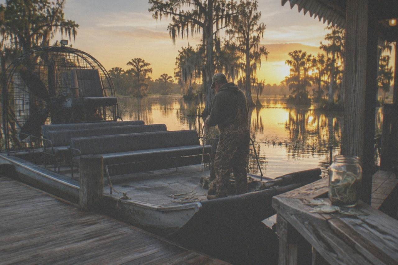 an airboat resting at a wooden swamp dock with cypress trees and still water behind it