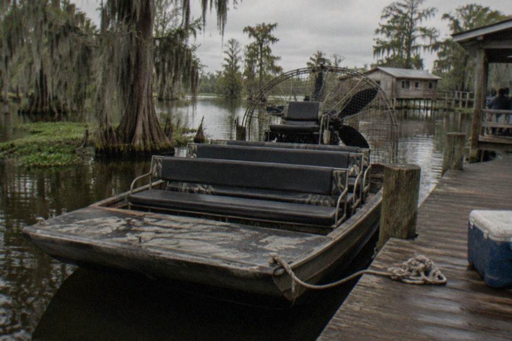 a weathered airboat docked beside cypress trees in a still bayou
