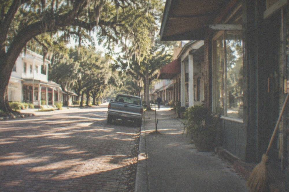 A quiet Louisiana small town street with oak trees and storefronts in morning light