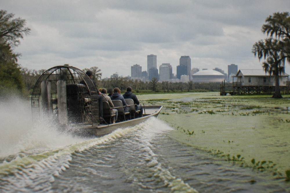 A flat-bottomed airboat with a large rear fan cruising fast across open swamp water