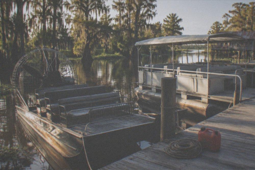 An airboat and a covered pontoon moored side by side at a swamp tour dock