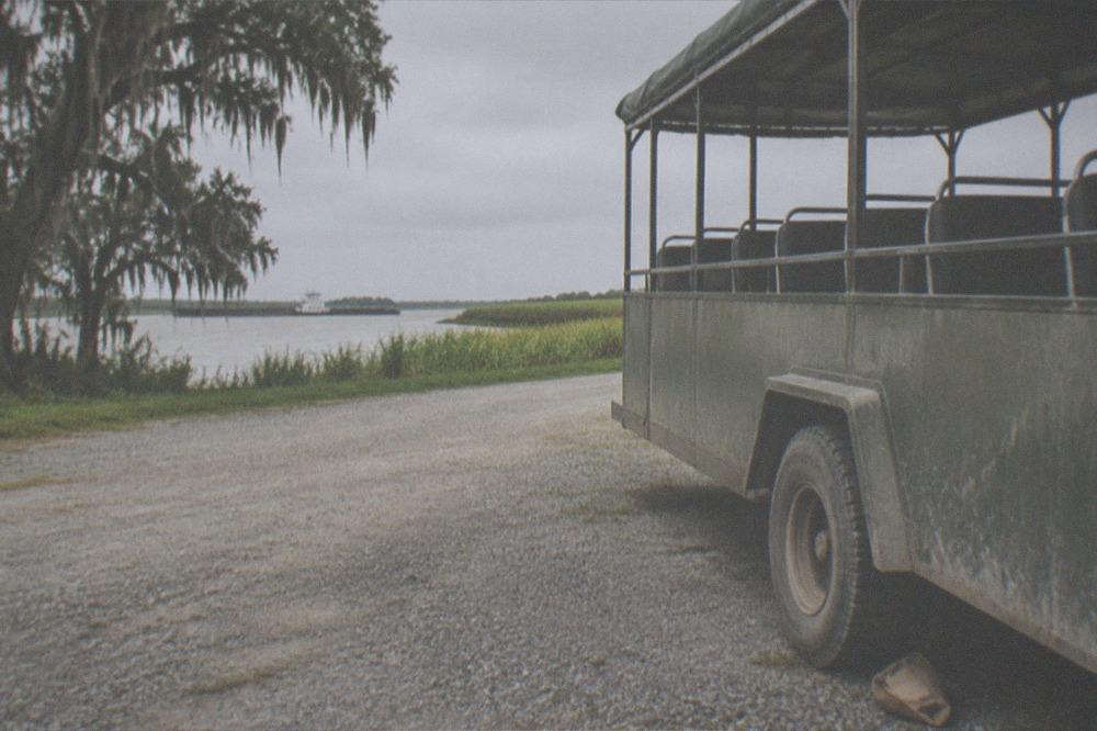 Tour bus parked on a gravel road beside a levee with fields beyond