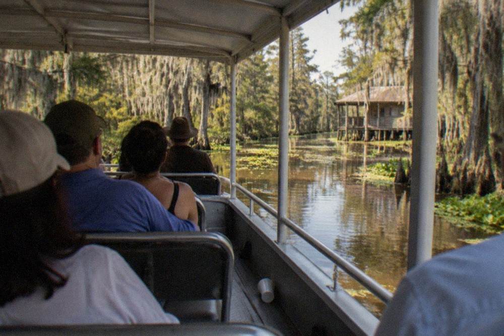 Passengers seated under the canopy of a covered pontoon boat cruising a narrow swamp channel